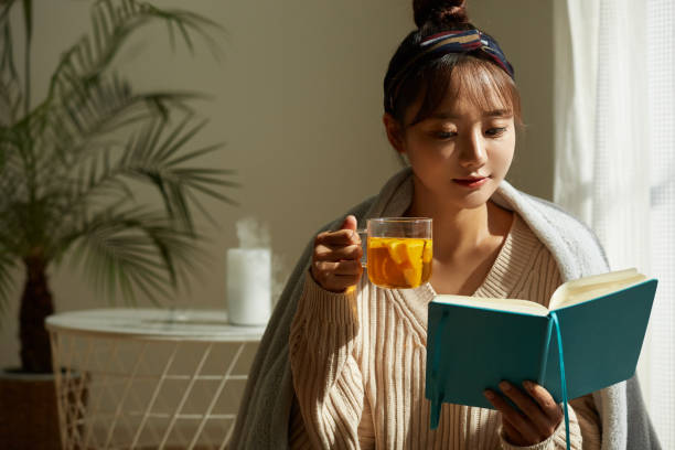 フルーツティーを飲みながら家でリラックスしている若いアジアの女性 ストックフォト